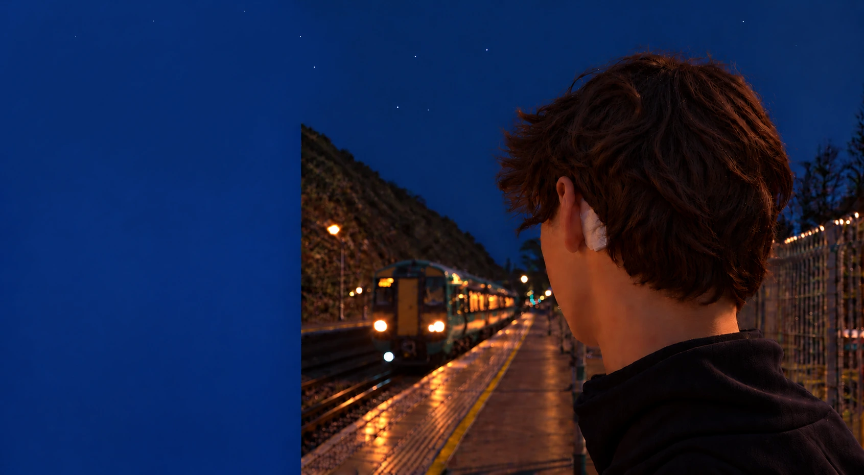 A commuter on a night-time station platform wearing the Excito earpiece as a train approaches